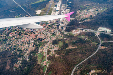 View from the window of a flying plane on the city, roads, green forest