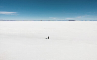 Isolated tourist enjoying endless infinite vastness dreamy landscape of white salt flat lake Salar...