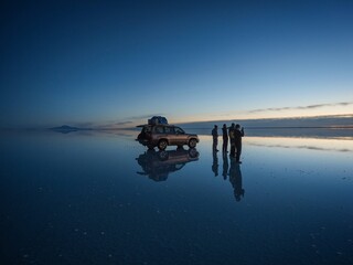 Tourist group with offroad car SUV on Salar de Uyuni salt flat lake in Bolivia andes mountains...