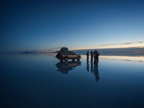 Tourist group with offroad car SUV on Salar de Uyuni salt flat lake in Bolivia andes mountains sunrise mirror reflection