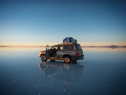 Offroad car SUV jeep of tour group on Salar de Uyuni salt flat lake in Bolivia andes mountains sunrise mirror reflection