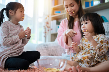A mother with two children sitting in the living room eating snacks. A mother with two young daughters had breakfast at home.