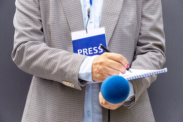 Female journalist at news conference or media event, writing notes, holding microphone