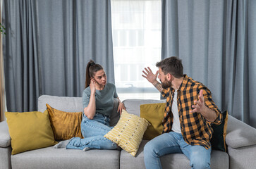Young couple woman and man sitting on the sofa in the living room had an argue with big fight where boyfriend spread his hands on the girlfriend, relationship issues
