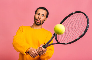 African american man playing tennis isolated over pink background. Studio shot of fit young player at studio in motion or movement during sport game.