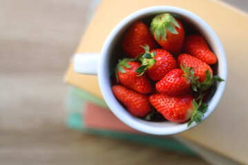 Mug filled with fresh strawberries and stack of book on a table. Top view.