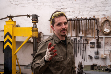 Portrait of a blacksmith against the background of machines and tools. The man is gesturing, looking at the camera.