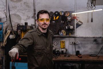 Portrait of a young modern artisan against the background of a blacksmith workshop, a man in protective yellow glasses and headphones