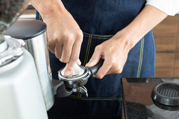 Closeup of Barista hand holding ground coffee for preparing coffee. Barista preparing portafilter before making caffee in a cafe shop. Barista holding portafilter tamping  and preparing cup of coffee.