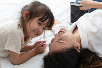 Mother and daughter are playing together on the bed in the morning. Mother and daughter sitting on bed enjoy quality time playing game together during home quarantine.