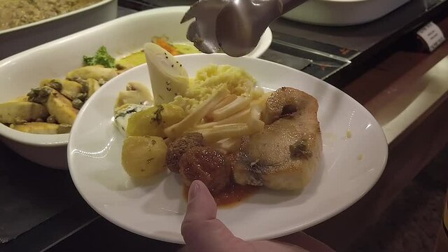A delicious meal on a a buffet restaurant which allows you to eat as much as you can. Fries, fish, meatball, palm heart and potatoes are being served by a hand with plastic glove
