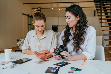 Fototapeta premium Two young women selecting photos on the camera indoor