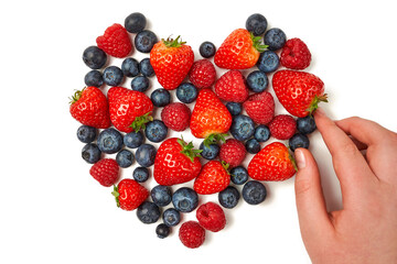A child is making a heart from blueberries, strawberries and raspberries on a white background.