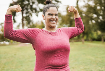 Plus size woman at city park posing showing biceps muscles - Curvy girl after sport workout outdoor