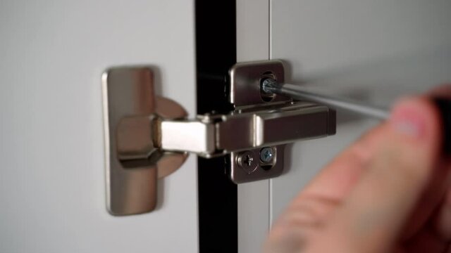 Close up shot the master twists the screw of the hinge of the Cabinet door in the kitchen. Installation and adjustment of kitchen Cabinet doors. 4K