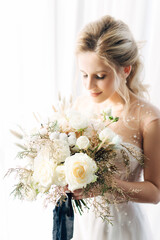 Delicate portrait of the bride with soft focus. A woman holds a wedding bouquet of roses and gypsophila in her hands. Floristry and flowers during the holidays. Wedding decor concept in light color.