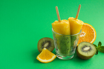 Popsicles with kiwi and orange fruit on the green background. Copy space.