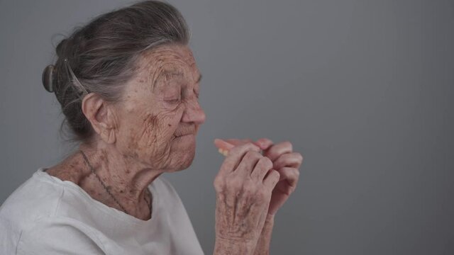 Dental concept. Elderly female 90 years old inserts denture. Senior woman gray hair using dental prosthesis on gray background. Old patient fitted artificial jaw in studio. Flexible nylon denture