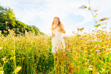 Fototapeta premium A joyful little girl runs around in a white dress with flowing hair in a yellow floor with flowers.