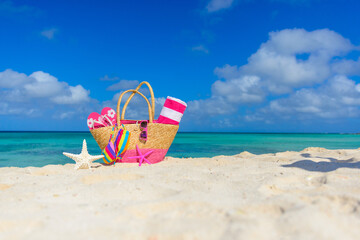 Colorful beach bag with sunglasses, towel, bikini and flip flops at the beach