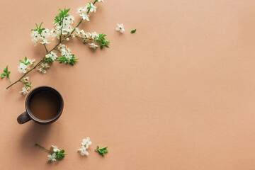 A cup of hot morning coffee and spring blooming branches on a beige background. View from above. Close up concept of holidays and good morning wishes 