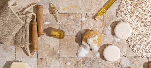 Zero waste bathroom accessories - soap, dry shampoo, exfoliating body strap, natural sea sponge with organic soap foam, wood brush, skin oil, mesh bag on earth toned stone tales top view 