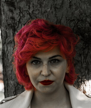 Mujer de pelo rojo y cara blanca sin saturaci&oacute;n , retrato de mujer resaltando el color rojo , mujer con la cabeza apoyada en un &aacute;rbol 