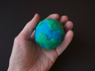 Hand holds a globe made of plasticine. Black background
