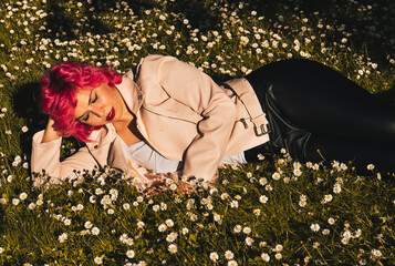 Mujer de pelo rosa tumbada sobre margaritas , descansando en el césped , durmiendo en el parque,...