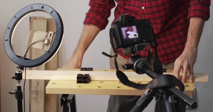 Vlogging, DIY guy fixing and securing wood plank onto woodworking workbench, recording it using smartphone with ring-light and digital slr camera, real people, close up
