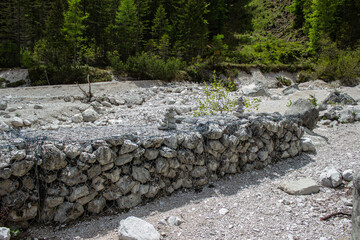 Metal mesh with stones inside for an anti-erosion intervention. Protection against alluvial water on the river bed in the middle of the alpine forest. Val d'Oten, Calalzo di Cadore, Italy