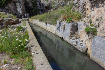 Ancient canal dug into the rock by the Etruscans. Ancient canal with murky water in the middle of the vegetation. Tagliata Etrusca, Ansedonia, Italy.