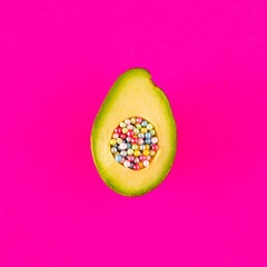 Sliced avocado on  intense pink background. In the indentation instead of a stone there are pearls...
