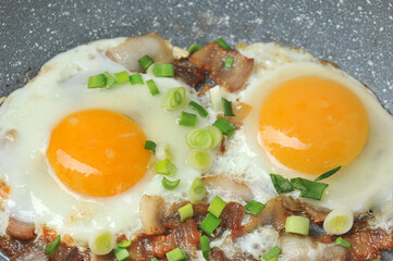 fried eggs with bacon and green onions in a frying pan