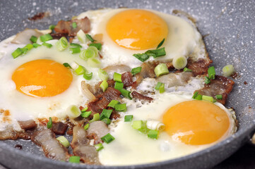 fried eggs with bacon and green onions in a frying pan
