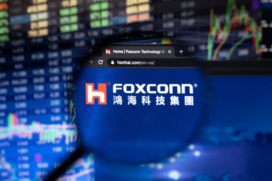 Hon Hai Precision Industry company logo on a website with blurry stock market developments in the background, seen through a magnifying glass