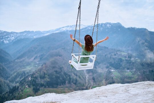 Free Woman Traveler With Open Arms Enjoying Of Swinging On A Heavenly Swing And Mountain View. Calm And Quiet Wanderlust Concept Moment When Person Feels Happiness And Freedom