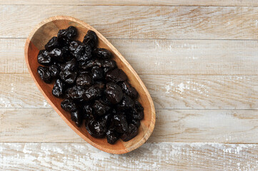 prunes in a wooden plate on a wooden background