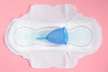 Menstrual cup lies on a pad on a pink background. Concept of choosing an ecological product that is safe for the environment. 
