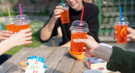 Schoolgirls celebrate having an aperitif.
Girls cheer with takeaway spritzes with different colored straws. Happiness and celebration after the lockdown.