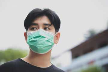 Portrait Close- up  of Asian man wearing Face Mask protect spread Covid-19 Coronavirus , in the background of an open- air building.
medical face mask that protects against the spread  disease. 