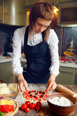Woman in white shirt and apron putting the ingredients on the pizza. Pizza concept. Production and delivery of food