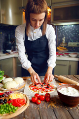 Woman in white shirt and apron putting the ingredients on the pizza. Pizza concept. Production and delivery of food