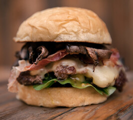 Fast food. Delicious gourmet burger. Closeup view of a meat hamburger with mushrooms, cheese, bacon, arugula and mustard, on the pub wooden table.