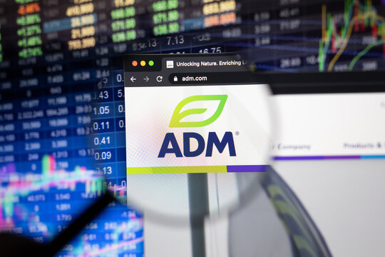 ADM company logo on a website with blurry stock market developments in the background, seen on a computer screen through a magnifying glass