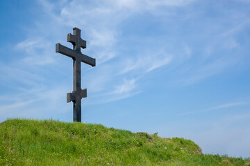Huge metal dark gray cross on the mountain against the blue sky. Summer day. Faith and hope concept.