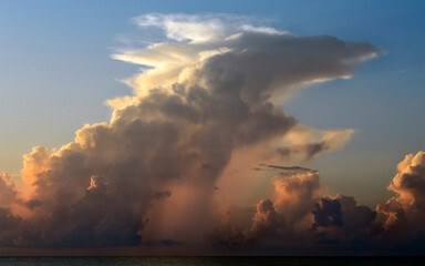 Morning  sun shining through thunder clouds shaped like an animal and shedding rain over the ocean