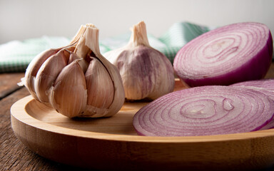 Garlic and red onion on a wooden plate over rustic wood, black background, selective focus.