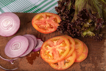 Fototapeta na wymiar tomatoes, red onion and red lettuce in detail on wood over checkered tablecloth, selective focus.