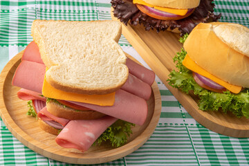 sandwiches placed on a wooden plate on green and white checkered tablecloth, light background, selective focus.